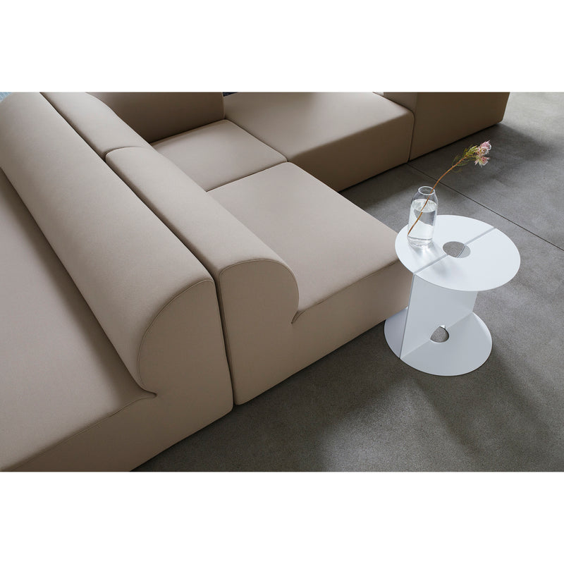 A minimalist living room showcases an Objekte unserer Tage Weber Modular Sofa and a sleek white round side table adorned with a glass vase holding a pink flower. A neutral-toned rug completes the space, adding German sensuality.