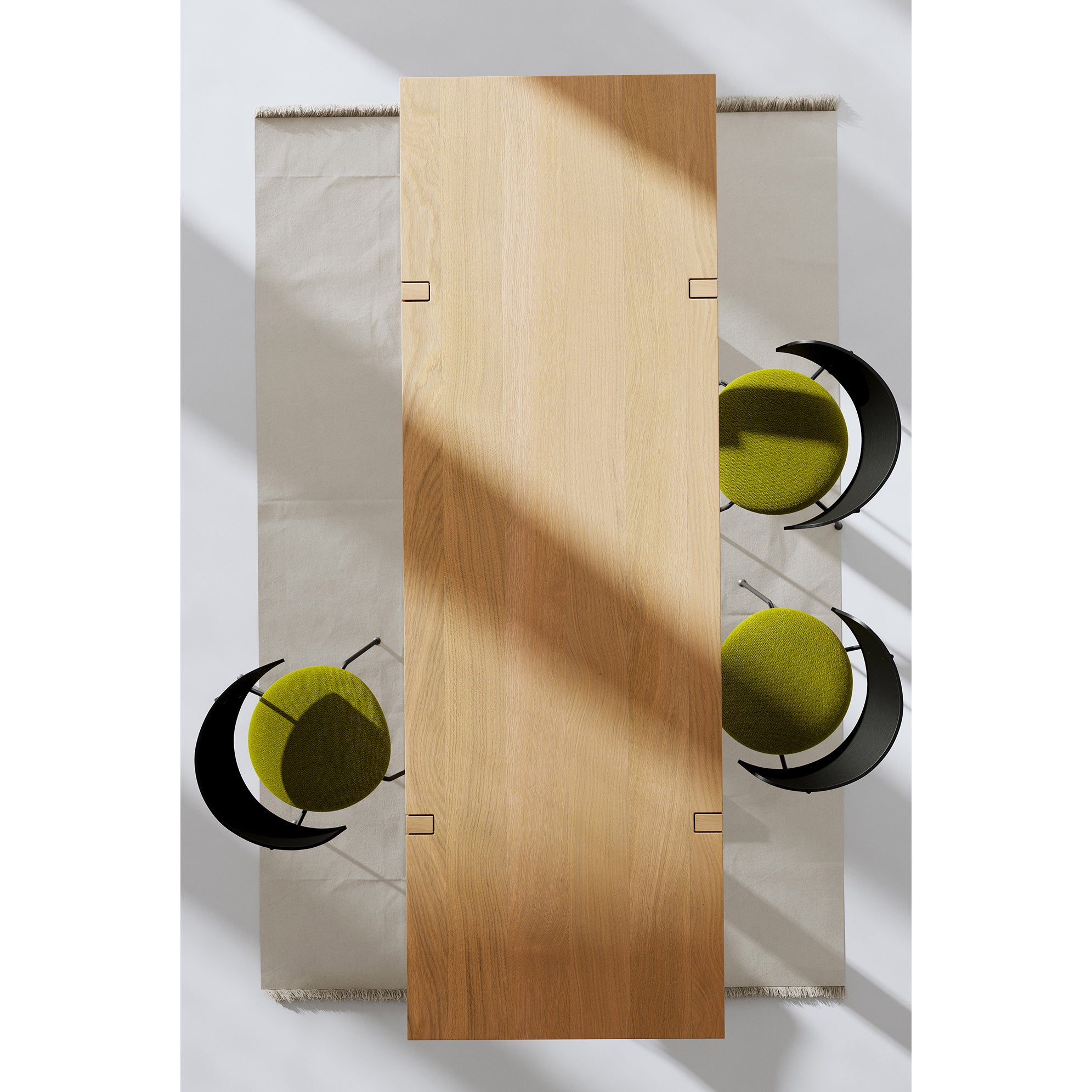 From above, see a Richter Table by Objekte unserer Tage with three green-cushioned chairs on a light rug. The handcrafted black curved frames of the chairs are artistically highlighted as natural sunlight casts soft shadows on this sustainable forestry masterpiece.