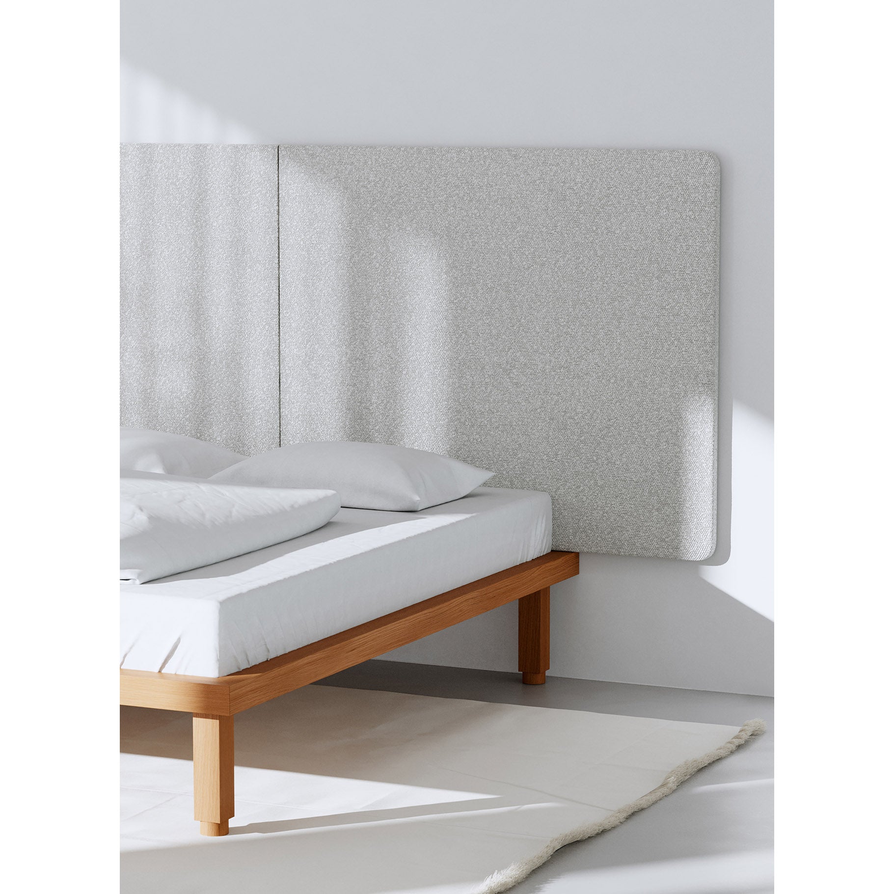 A minimalist bedroom showcases an Objekte unserer Tage Kaya Bed with a wooden frame, white bedding, and light gray upholstered headboard. Sunlight creates soft shadows on a cream rug. Made from sustainable materials for restful sleep, the scene exudes calm and order.