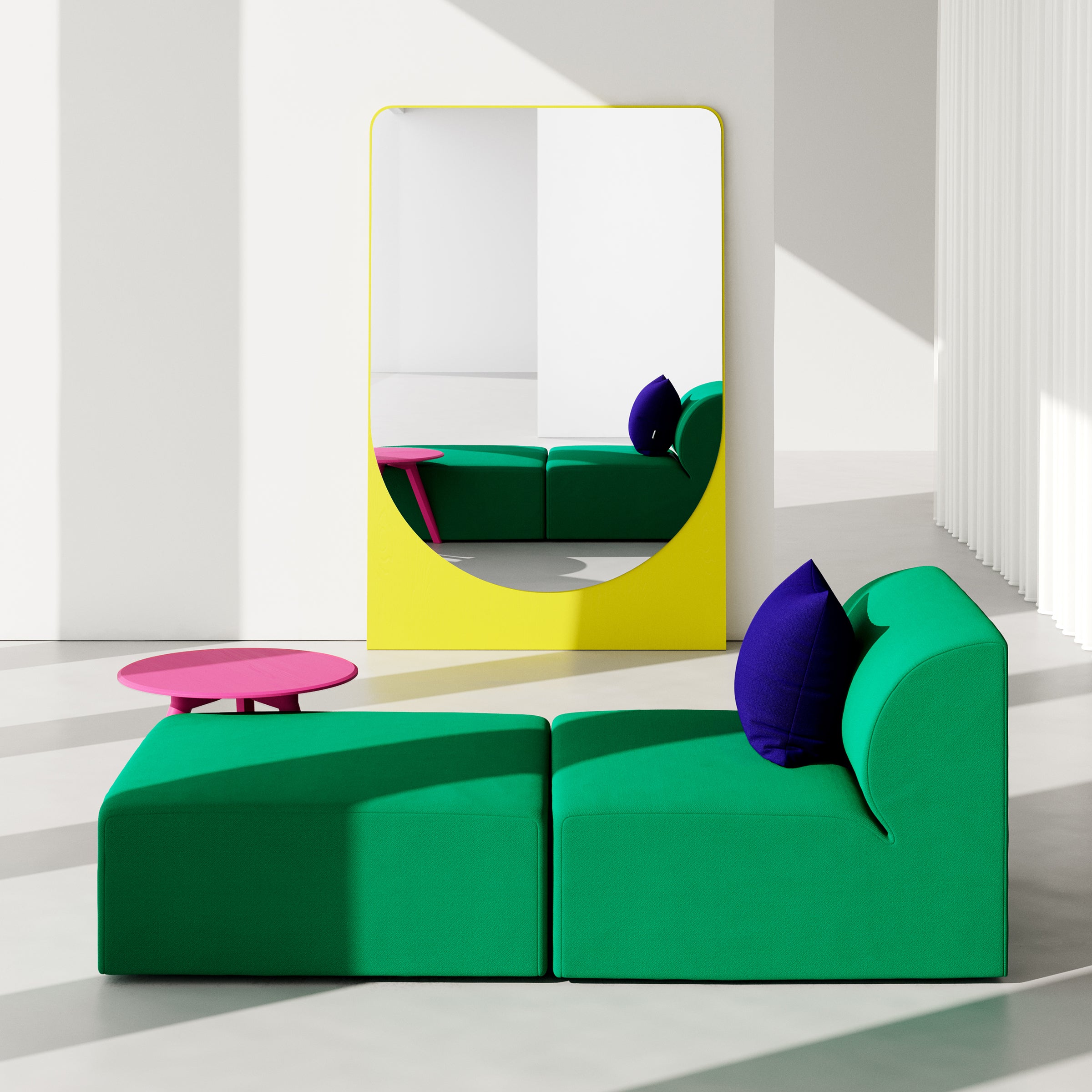 A modern living room showcases a green sectional sofa with purple cushions. Beside it, a round pink coffee table enhances the decor, while a large yellow-framed FRIEDRICH MAX Mirror by Objekte unserer Tage reflects its sculptural allure against white walls and bright lighting.
