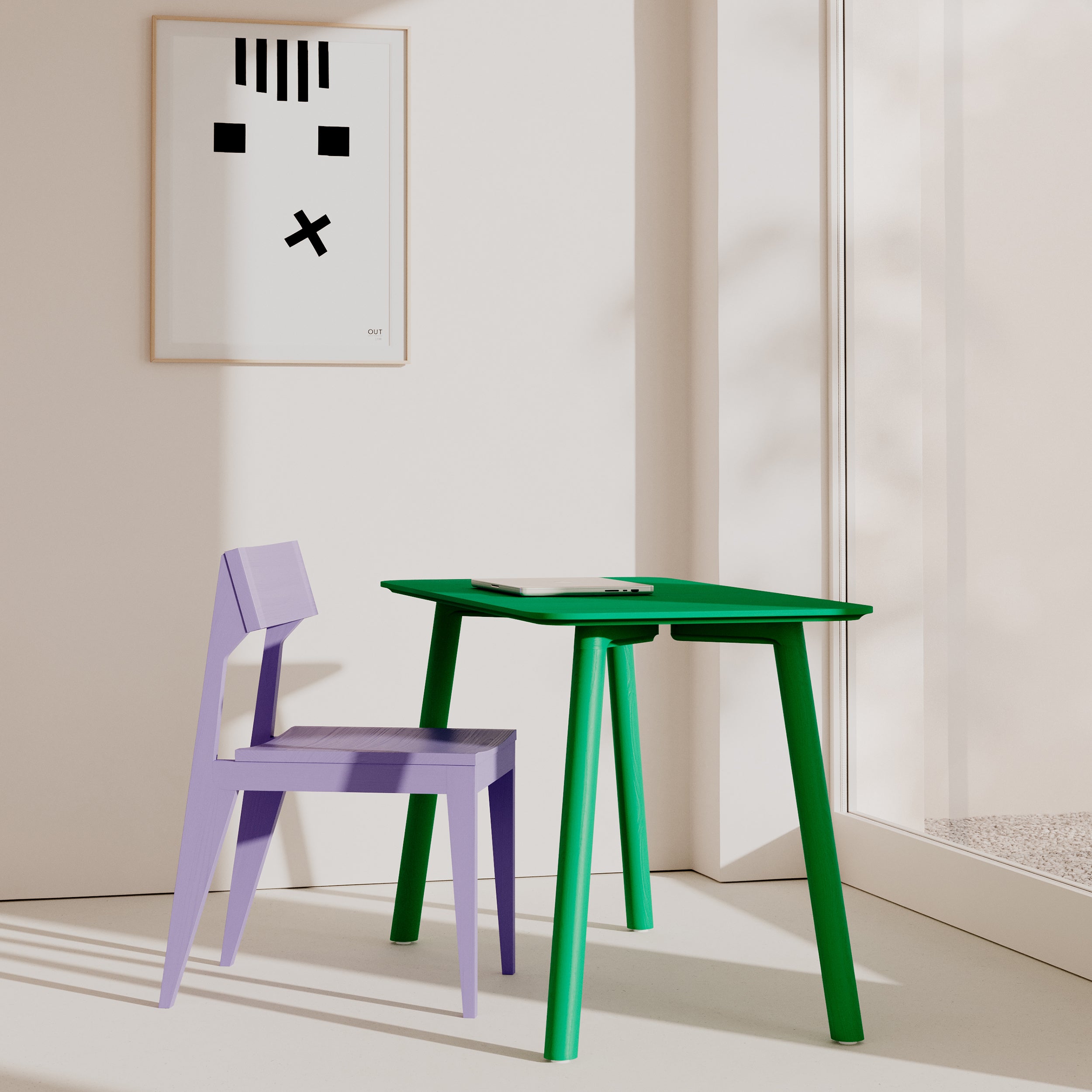A minimalist room includes the Meyer Color Table in green with an ash wood veneer by Objekte unserer Tage, paired with a light purple chair. A closed laptop rests on the table, and black and white abstract face artwork adorns the wall. Sunlight casts soft shadows through a large window.