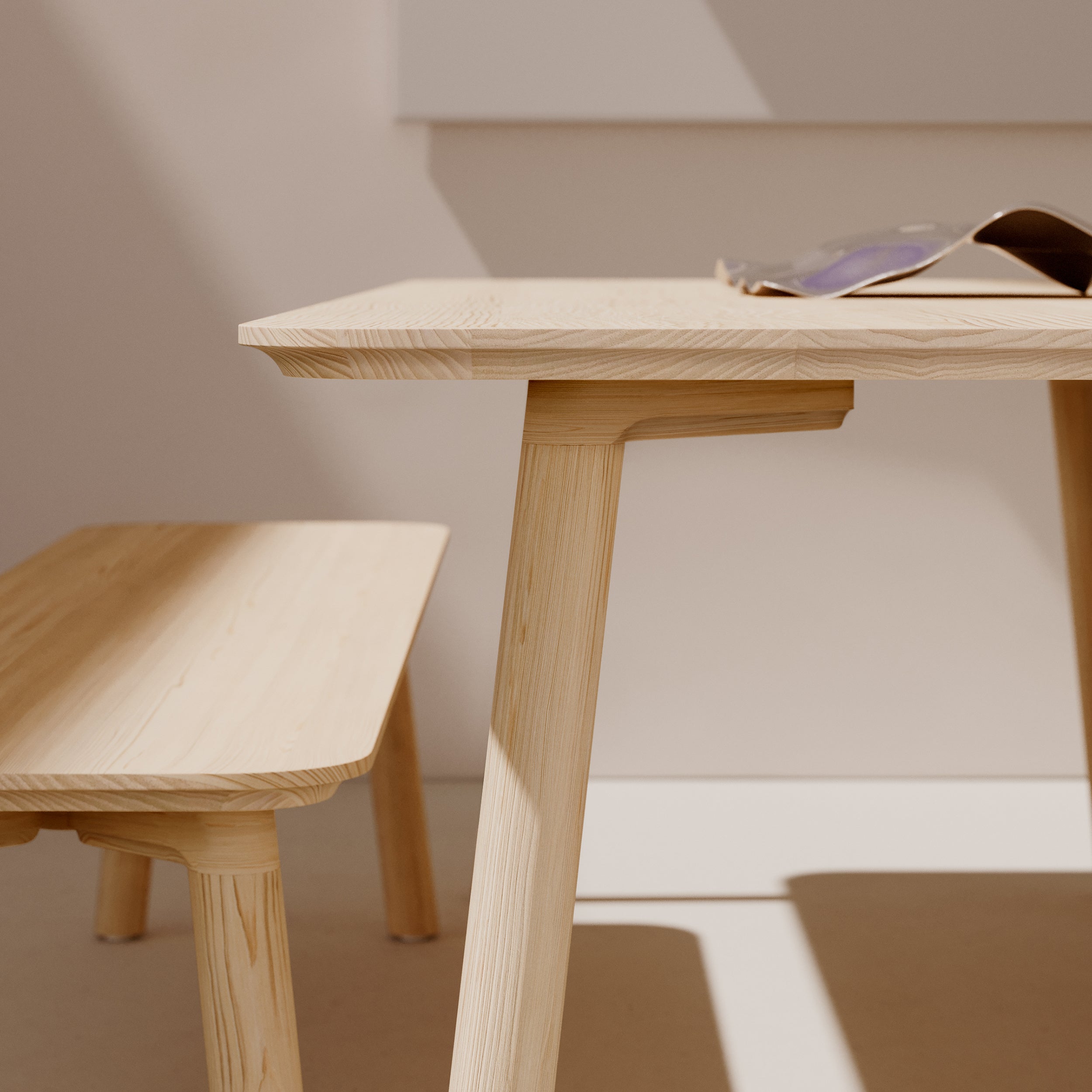 The solid wood table and Objekte unserer Tages Meyer 23 Bench beneath feature clean lines and a minimalist design. Sunlight casts soft shadows, enhancing the smooth texture. An open magazine on the table hints at sustainable forestry practices behind its creation.