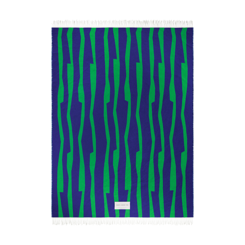Presenting the SEIDEL Throw by Objekte unserer Tage: a rectangular organic cotton textile featuring green and dark blue vertical zigzag patterns with short fringes on the top and bottom, plus a small white label near the bottom center.