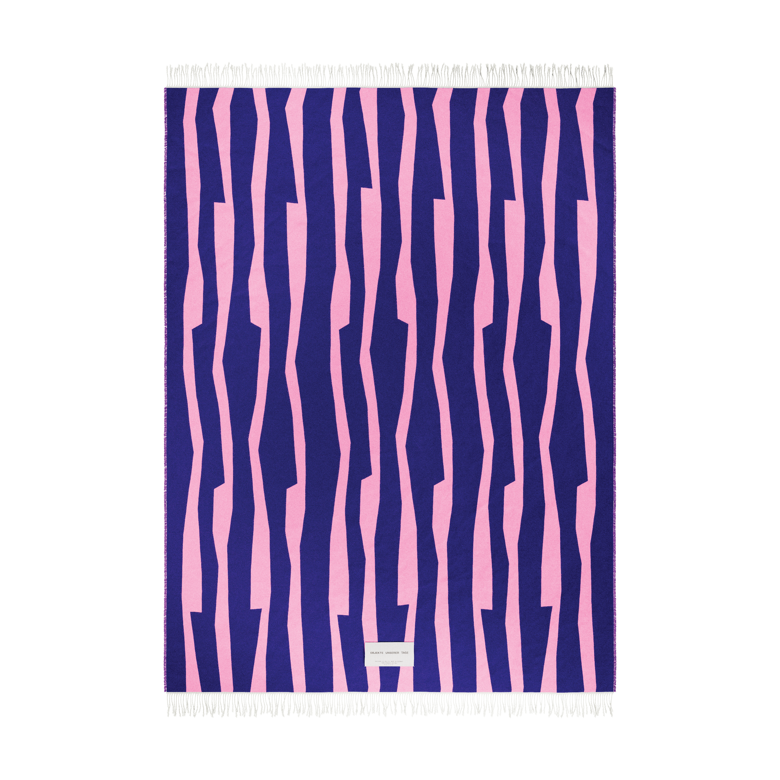 The SEIDEL Throw from Objekte unserer Tage is a rectangular textile made of organic cotton, featuring fringe edges and an abstract graphic design with irregular pink stripes on a dark blue background, along with a small white label at the bottom center.