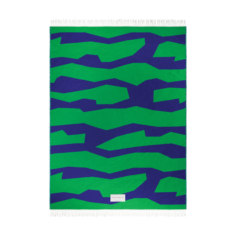 Introducing the SEIDEL Throw by Objekte unserer Tage, a fringed organic cotton textile with abstract graphics, showcasing bold green and blue jagged stripes and a subtle white label at the bottom center.
