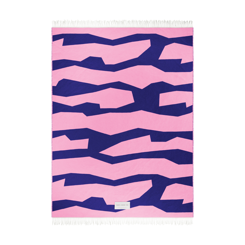 The SEIDEL Throw by Objekte unserer Tage is a rectangular textile crafted from organic cotton, featuring abstract navy jagged stripes on a pink background. It includes white fringes at the top and bottom, with a small white label near the bottom center.
