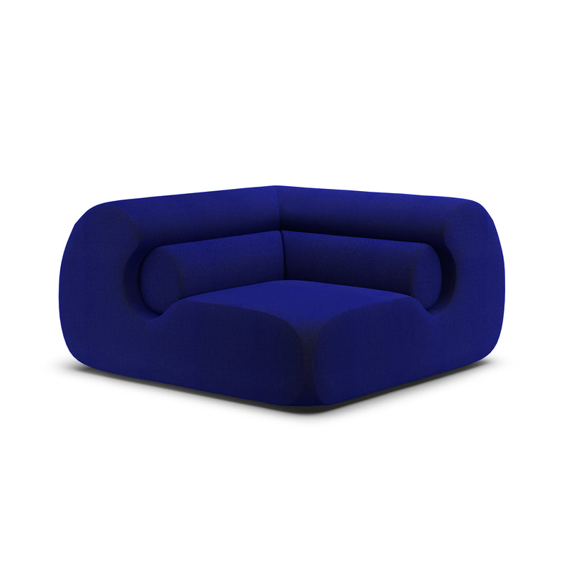 The Ola Sofa by Objekte unserer Tage is a modern deep blue velvet armchair reminiscent of the Mediterranean Sea, boasting a bold, rounded design with thick memory foam cushions and seamless upholstery for a stylish, cozy look on a white background.