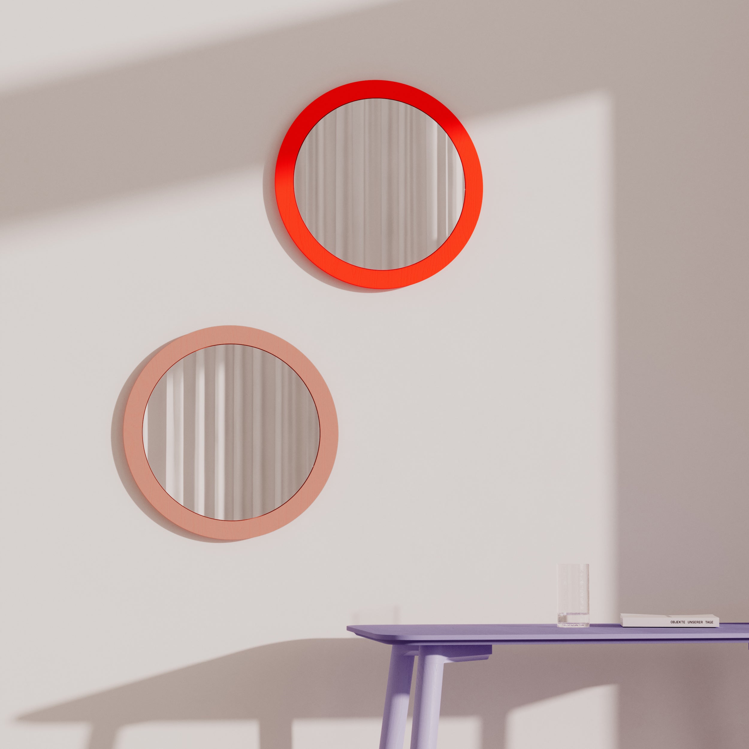 The Lorenz Mirror collection by Objekte unserer Tage includes two round mirrors with vivid red and peach borders on a white wall, highlighting a striking geometric design. Sunlight creates diagonal shadows, enhancing depth. Below, a purple table with a glass and small object is partially visible.