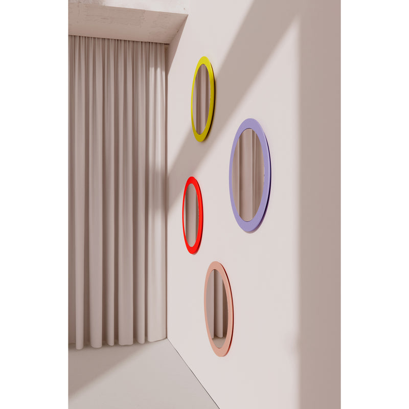 The Lorenz Mirror collection by Objekte unserer Tage features four circular mirrors with vibrant frames in yellow, red, lavender, and peach on a white wall. Beige curtains to the left enhance the modern artistic design with shadows, embodying a contemporary aesthetic.
