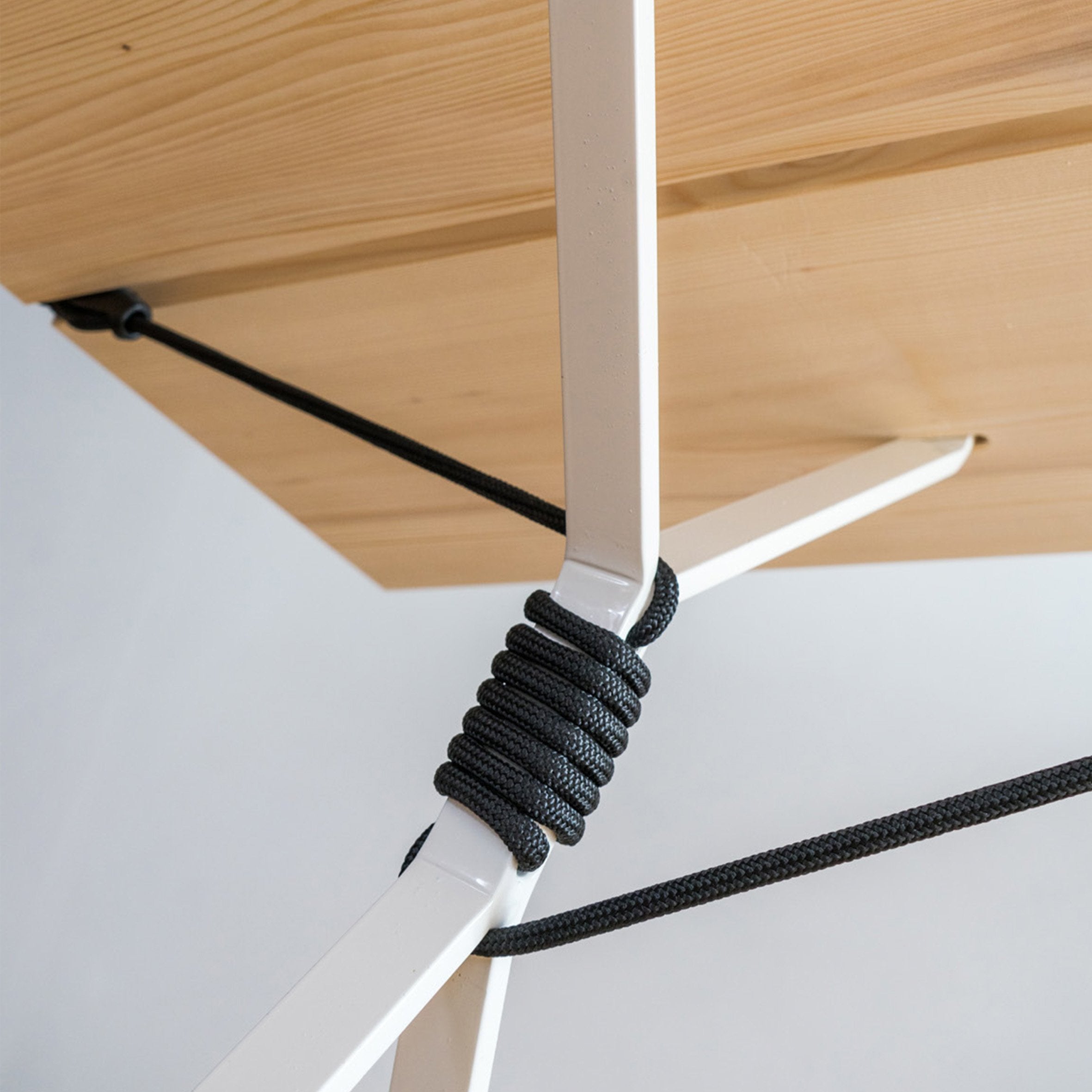 A close-up of the Kampenwand Table by Moormann shows its white metal legs with black cords wrapping tightly around where the leg meets the table, showcasing a unique design element in Nils Holger Moormanns style. The background is plain and white.